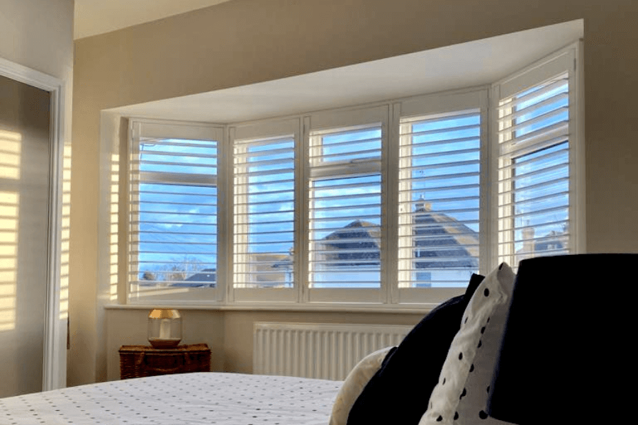 bespoke window shutters installed in a bay window in a bed room